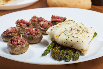 Cod dish on green asparagus, accompanied by mushrooms stuffed with ham.