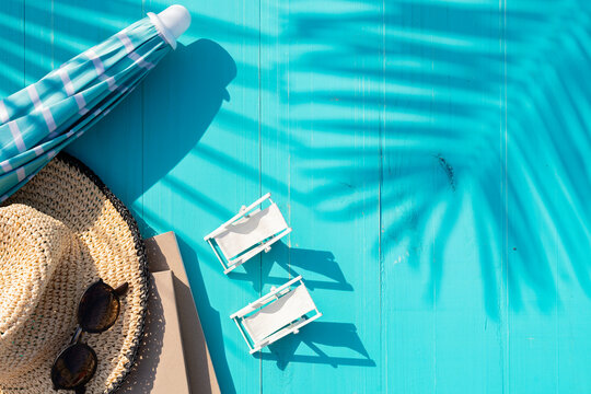 Composition view from above made with books, sunglasses, umbrella and beach hat on background of turquoise painted planks with shadow of palm leaves