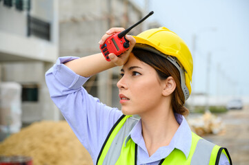 Young construction engineer woman wearing safety helmet wipes sweat on her face. Tired heat and hot at building construction site. - obrazy, fototapety, plakaty