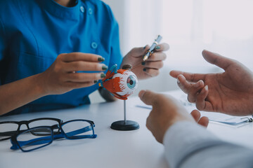 Close-up of Asian female doctor talking with elderly patient showing eyeball model and explaining...