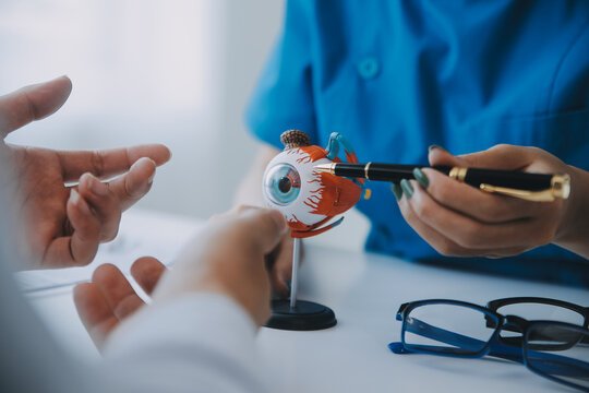 Close-up of Asian female doctor talking with elderly patient showing eyeball model and explaining eye disease in hospital