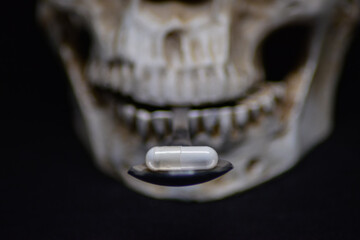 Eine Pille liegt auf einem Löffel der von den Zähnen eines Schädels gehalten wird auf schwarzen...
