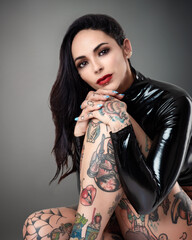 Portrait of beautiful tattooed Goth model with lip studs wearing black PVC body suit