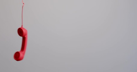 Vintage phone hanging in air after call ended. Red wire telephone receiver dangling and swinging to and fro in oscillatory motion on grey background making us worry, leaving uneasy uncertain sensation