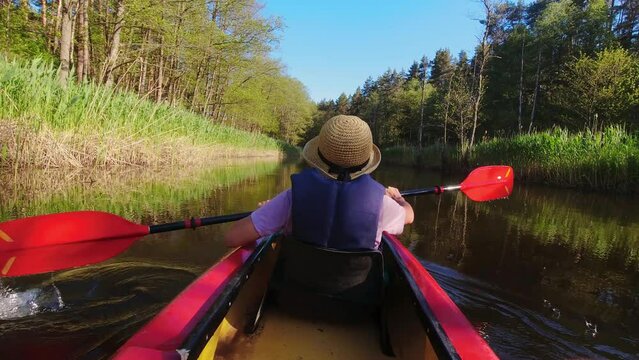 Back Rear View strong caucasian woman rowing Kayaking In Beautiful Lithuania countryside river - Zemeina. Action Camera POV Of Girl Paddling On canoe. Active holidays fun outdoors
