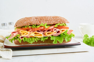 Sandwich. One fresh big submarine sandwich with ham, cheese, lettuce, tomatoes and microgreens on light background. Healthy breakfast theme concept, school lunch, breakfast or snack.