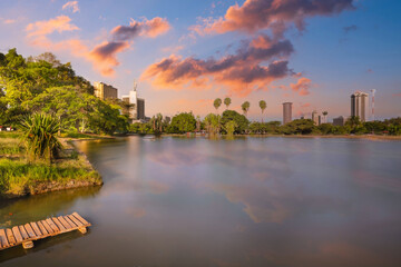 Golden Sunrise or Sunset at Urban Park with Calm Water, Reflective Skyline, and Lush Greenery