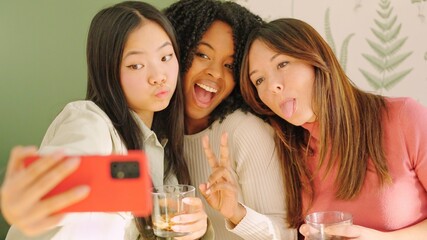 Multiracial women pulling funny faces while taking a selfie indoors