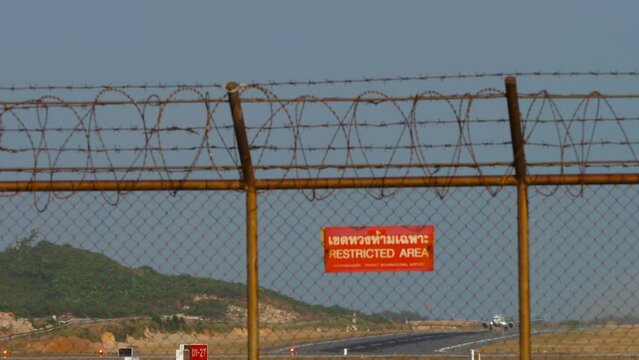 Airport fence with red Restricted Area sign. Jet plane with an unrecognizable livery taking off and climbing, front view, long shot