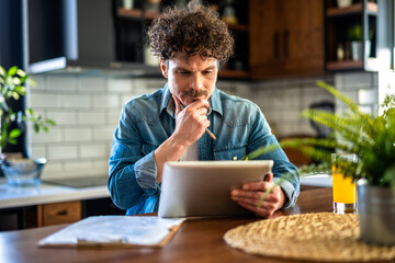 Latino Man In Kitchen Working From Home Using Digital Tablet