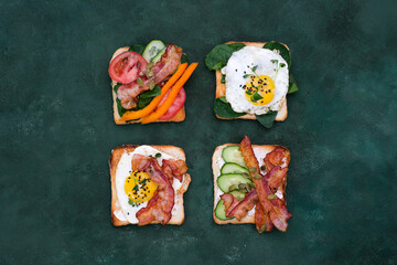  Sandwiches with fried eggs, fried ham, tomatoes, cucumbers, pepper on dark green background, top view.