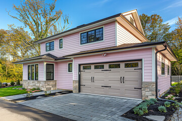 A newly built high-end home, modern in design, with a two-car garage, wrapped in soft pink siding and accented with a natural stone wall trim.