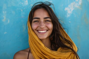 Portrait of a joyful young woman with a yellow scarf, smiling against a blue textured background.