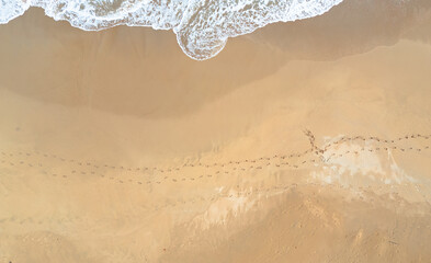 Footprints of people in the golden sand of a beach. Aerial view. Waves on the beach. Drone...