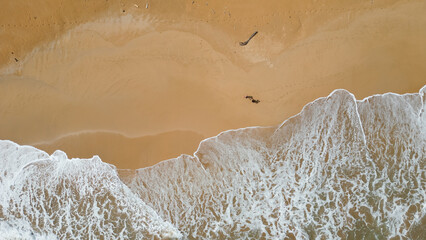 Couple walking on a golden sand beach. Aerial view. Waves on the beach. Footprints marked in the...