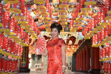 Portrait pretty Asian female in red traditional Chinese costume holding a fan standing and posing in front of the lanterns in the shrine.