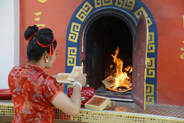 A pretty Asian woman burns paper for worship at the gold and silver paper burned stove.