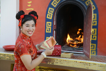 A pretty Asian woman burns paper for worship at the gold and silver paper burned stove.