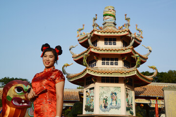 Portrait of a beautiful Asian woman in a red Chinese dresses pose and standing in front of Cinese pagoda inside a shrine.