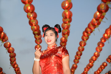 Portrait pretty Asian female in red traditional Chinese costume standing and posing in front of the lanterns in the shrine.