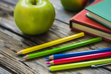 A green apple sits on a table next to a green notebook and a box of colored pencils