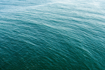 Aerial view of serene and tranquil blue ocean water with soothing waves creating abstract patterns and textures, perfect as a natural background for marine, maritime, and summer-themed designs