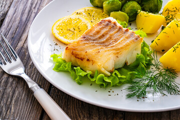 Fried cod loin, boiled potatoes and cooked Brussels sprouts on wooden table
