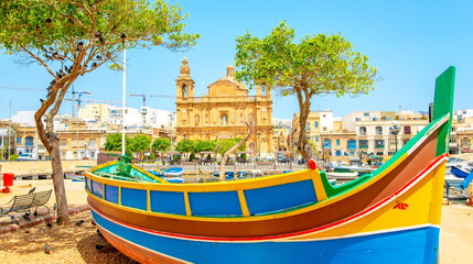 Maltese traditional colorful boat and Msida Parish Church on background, Malta