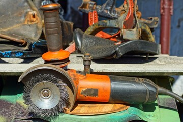 one powerful dangerous orange color with a metal round brush electric hand grinder lies on a green iron table on the street