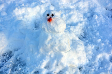 A beautiful little snowman made of white snow with orange carrots and black eyes. Snowman on the...