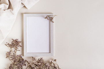 Empty photo frame, dried flowers and fabric on a light background top view