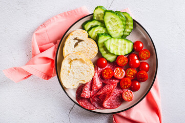 Close up of girl dinner of smoked sausage, cucumbers, cherry tomatoes and buns on a plate top view