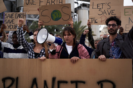 Diverse group of people gathered to protest against factories and pollution. Pro-earth demonstration with climate change banners.