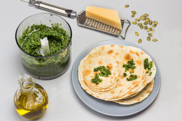Flatbread on ceramic plate. Grinded greens in blender.