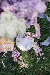 A greeting card with the inscription "Bonjour" lies on the grass, lilac flowers and a purple silk ribbon. Top view © Olga