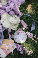 A greeting card with the inscription "Bonjour" lies on the grass, lilac flowers and a purple silk ribbon. Top view © Olga