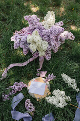 A greeting card with the inscription "Bonjour" lies on the grass, lilac flowers and a purple silk ribbon. Top view © Olga