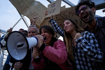 Woman shouting using a megaphone at an anti-war protest. People gathered with placards at a...