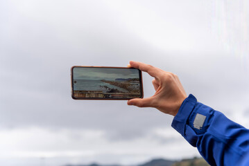 man's hand taking a picture of the landscape with his mobile phone and the cloudy sky in the background