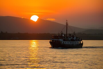 Fototapeta premium Boat glides under sunsets golden glow on Lake Baikal