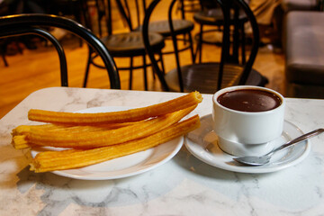 Traditional spanish dessert churros - fried choux pastry and hot chocolate mug on a table