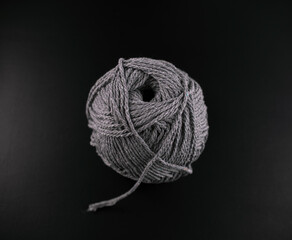 A grey ball of yarn sits on a black background. The yarn is unspun and he is a ball of wool