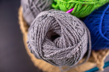 A basket of yarn with a gray ball of yarn in the center. The basket is filled with various colors of yarn, including green and blue. The gray ball of yarn is the main focus of the image