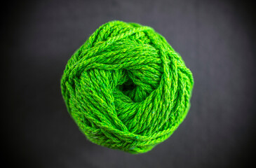 A green ball of yarn is sitting on a black background. The yarn is tightly wound and he is a skein...