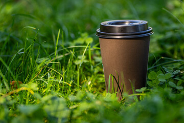 Takeaway hot coffee cup on green grass of park in summer day, meadow plants and mug in sunlight