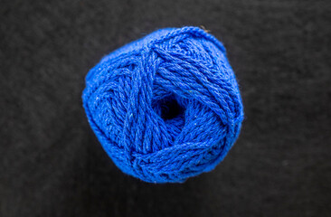 A blue ball of yarn sits on a black surface. The yarn is tightly wound and he is a skein of yarn
