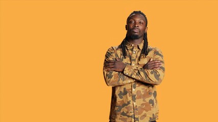 Portrait of guy with dreads smiling in studio set, wearing trendy camo clothes and feeling joyful...