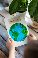 Children's craft for the Earth Day celebration. Little boy holding handmade simple postcard with a...