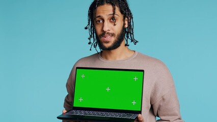 Joyous BIPOC man holding green screen laptop, having positive mood. Smiling person presenting chroma key notebook, doing recommendation, isolated over studio background, camera B