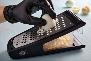 Egg chopped on a grater. Hands in black latex gloves rub a hard boiled chicken egg